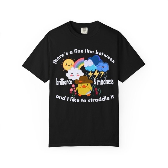 Graphic tee with cartoon duck holding a knife with its right-hand and flowers with its left-hand. Above the duck on the left side are cute cartoon sun and cloud with a half rainbow, and on the right side is a sad crying cloud with thunder and lightning. Surrounding this is the text: "there's a fine line between brilliance and madness and I like to straddle it". Front view color black.